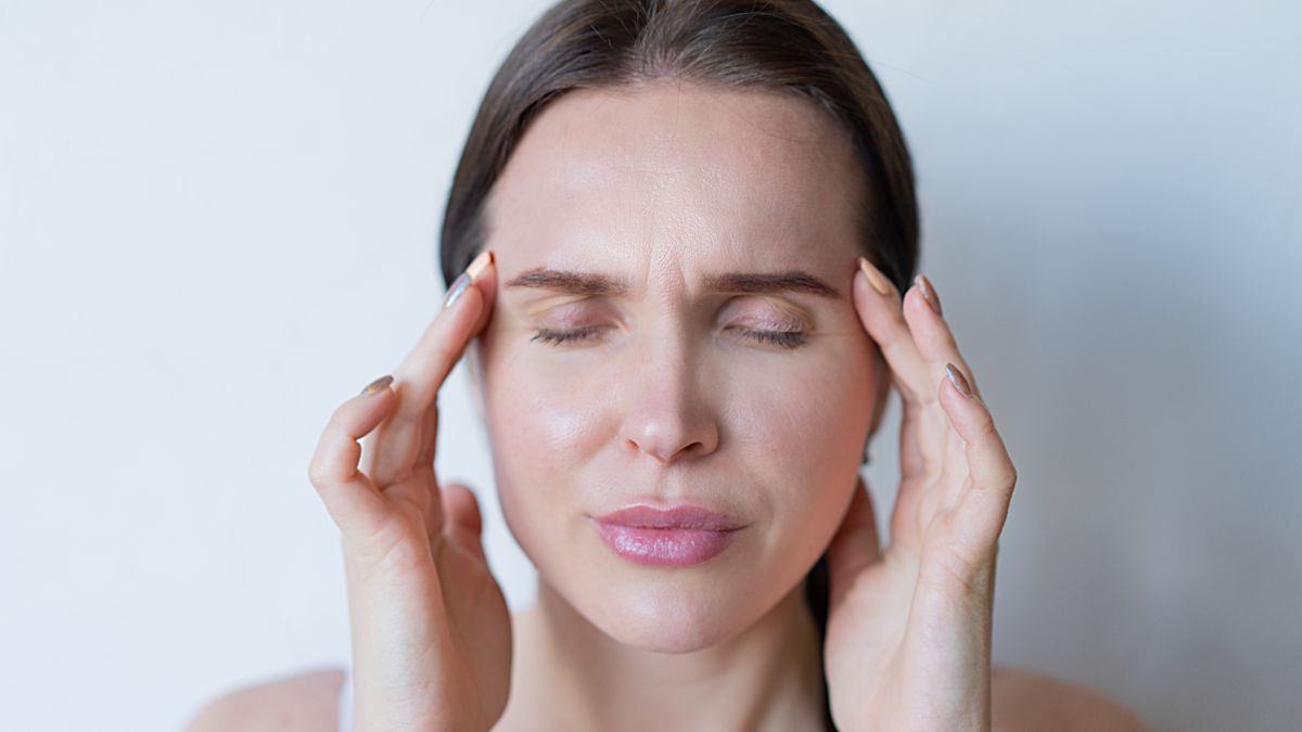 Woman with eyes closed pressing her fingertips to her temples and scalp, the sore, tender feeling behind many searches for trichologists Bournemouth near me