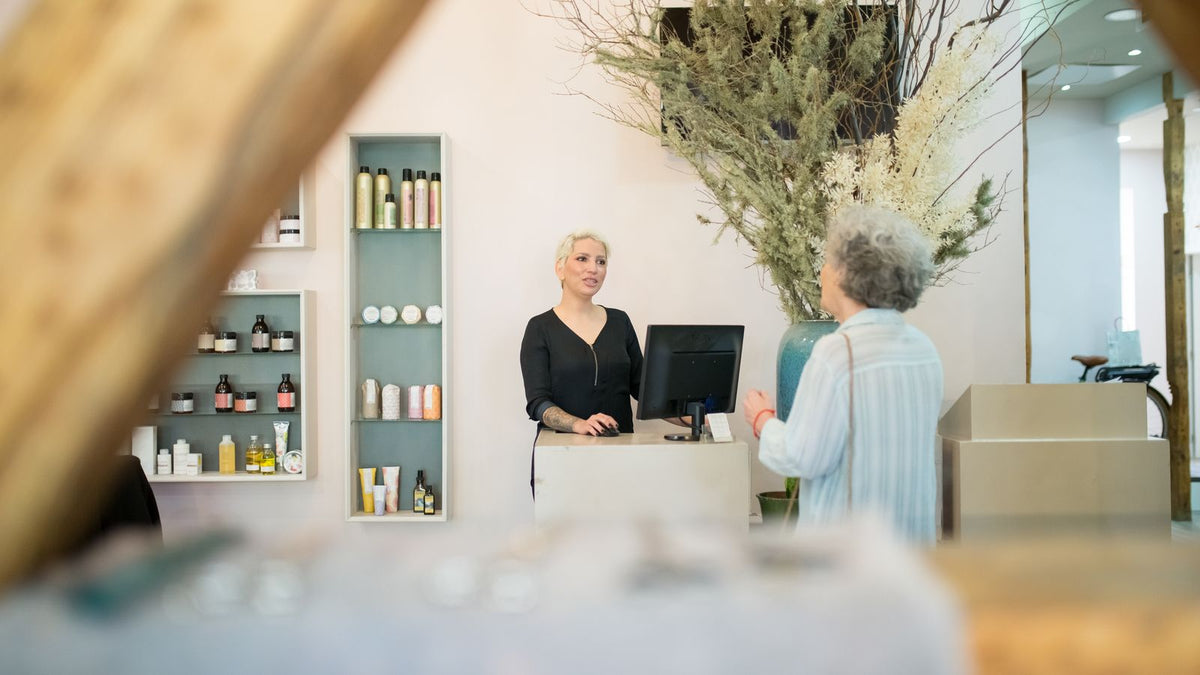 Woman talking with a hair professional at a salon reception desk, the kind of first conversation a trichologists Dunfermline search leads to