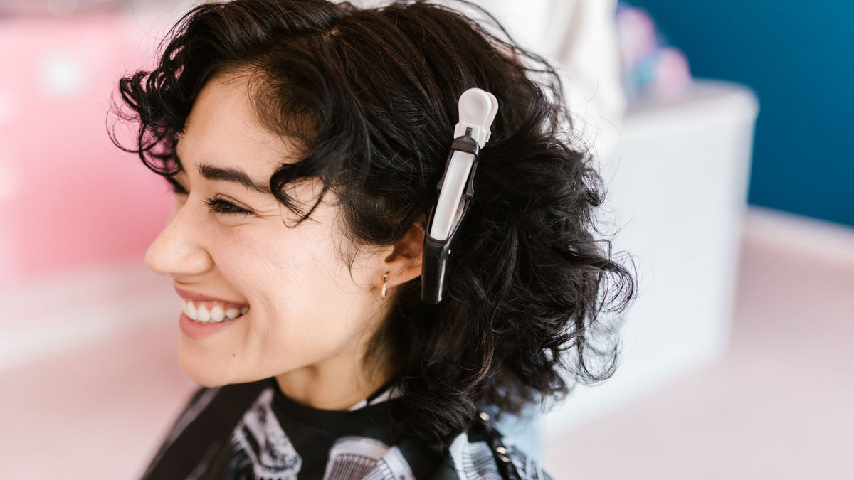 Smiling woman with soft curls in a hair salon, weighing up a perm on fine hair before searching trichologists Ellesmere Port