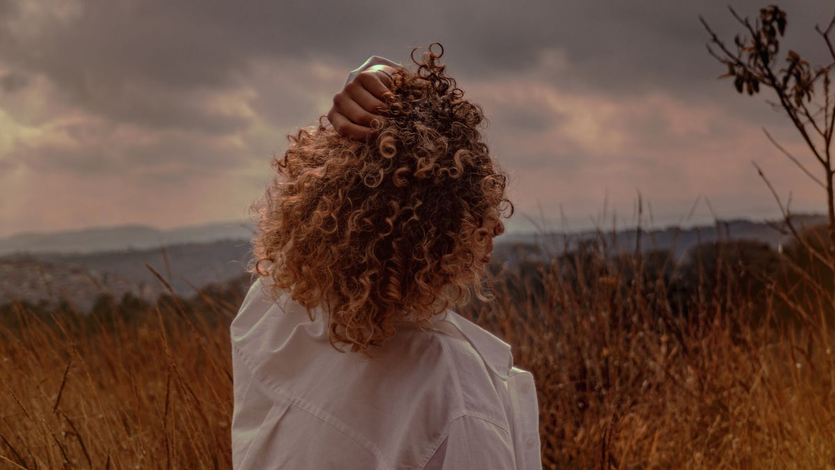 Woman touching her curly, frizz-prone hair under a cloudy sky, a common reason people search for trichologists Gloucester