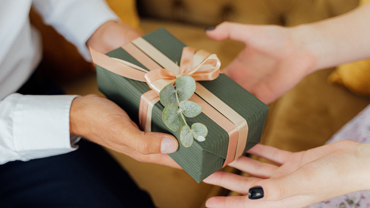 Hands passing a wrapped green gift box, a thoughtful present for someone with thinning hair, from a guide to trichologists in Shrewsbury