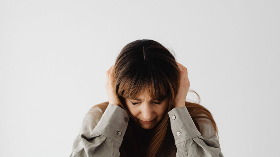 Woman holding her head with eyes closed, showing the stress that a trichologist in Guildford often links to sudden shedding